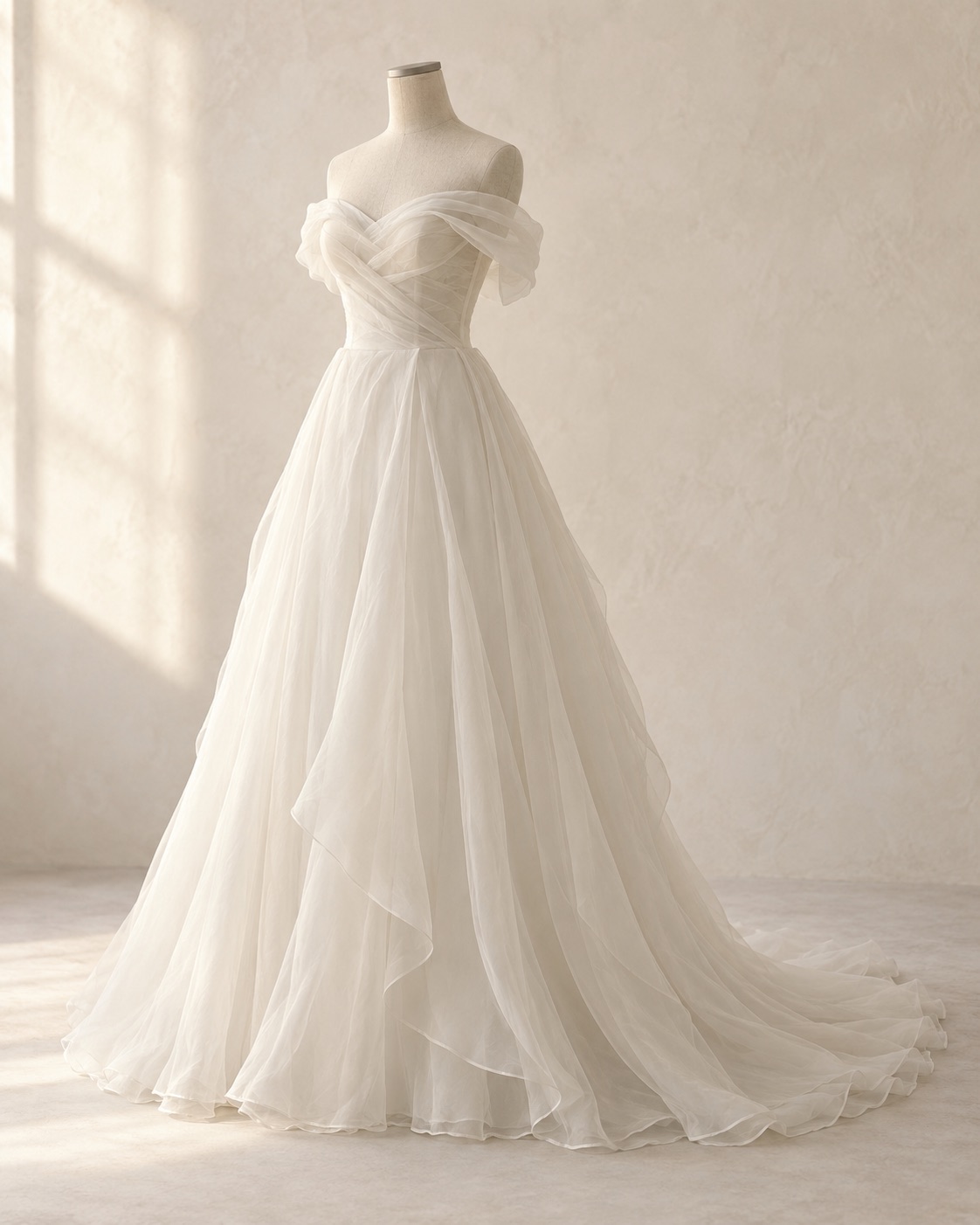Airy ivory organza with an off-shoulder neckline and a flowing skirt. Light layers give the silhouette movement.
